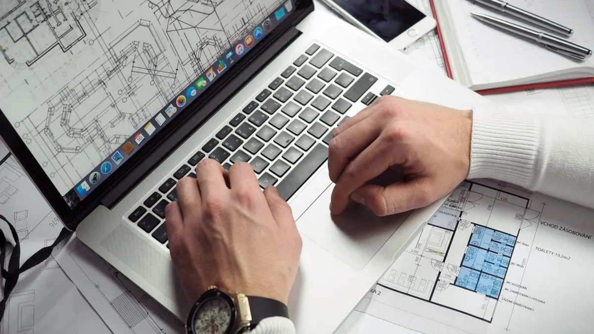 Someone planning a project on a laptop surrounded by drawings and notes, working out what it will cost